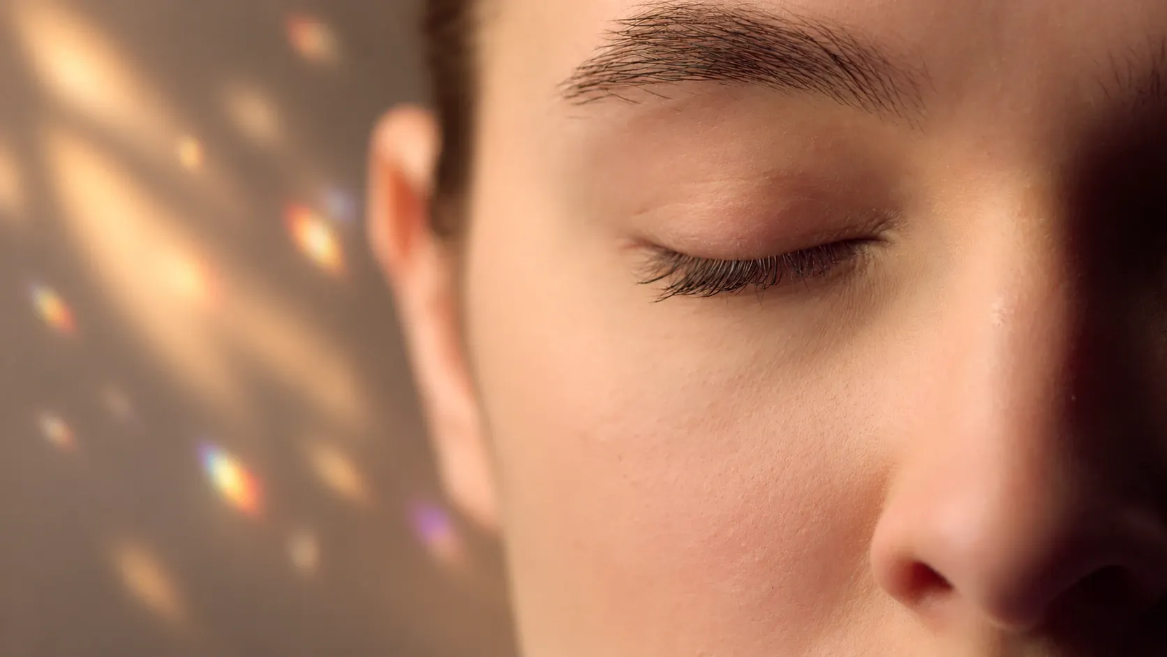 Close-up of a woman with her eyes closed, lit by warm amber light against a deep violet background