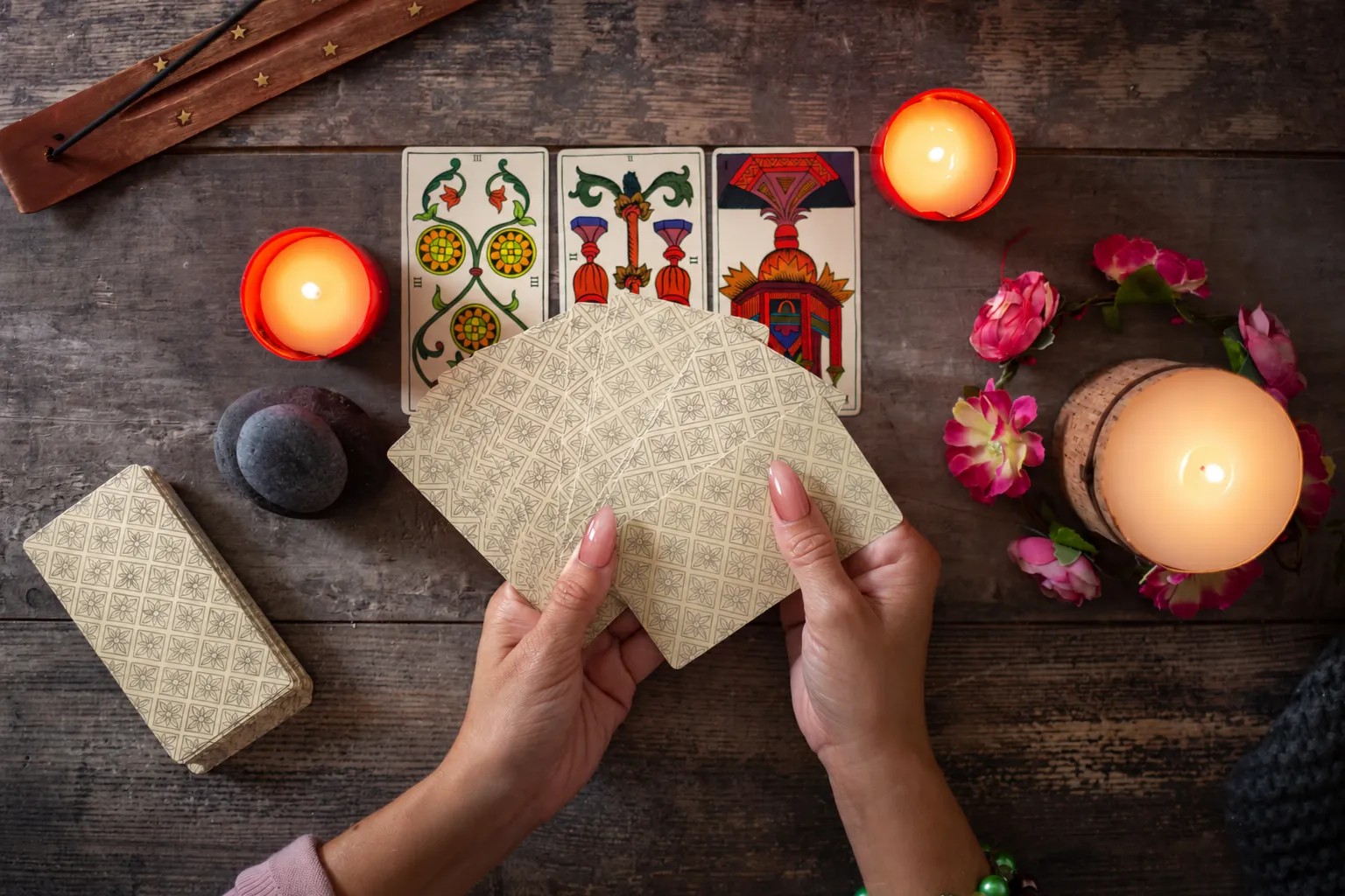 Hands fanning a tarot deck above three face-up cards, with candles around the table