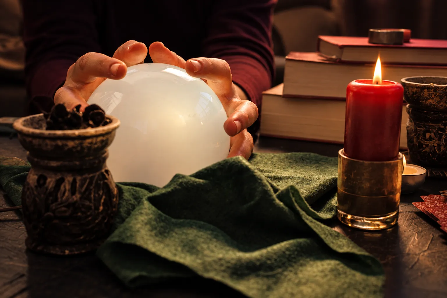 Hands resting around a crystal ball beside a lit candle